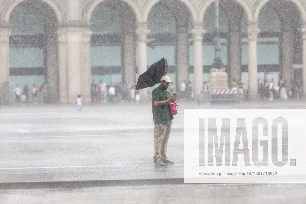 IPA86706245 - Milan, July 15, 2026, Piazza Duomo, summer thunderstorm, downpour, rain, people seeking shelter, tourists, umbrellas, wind
