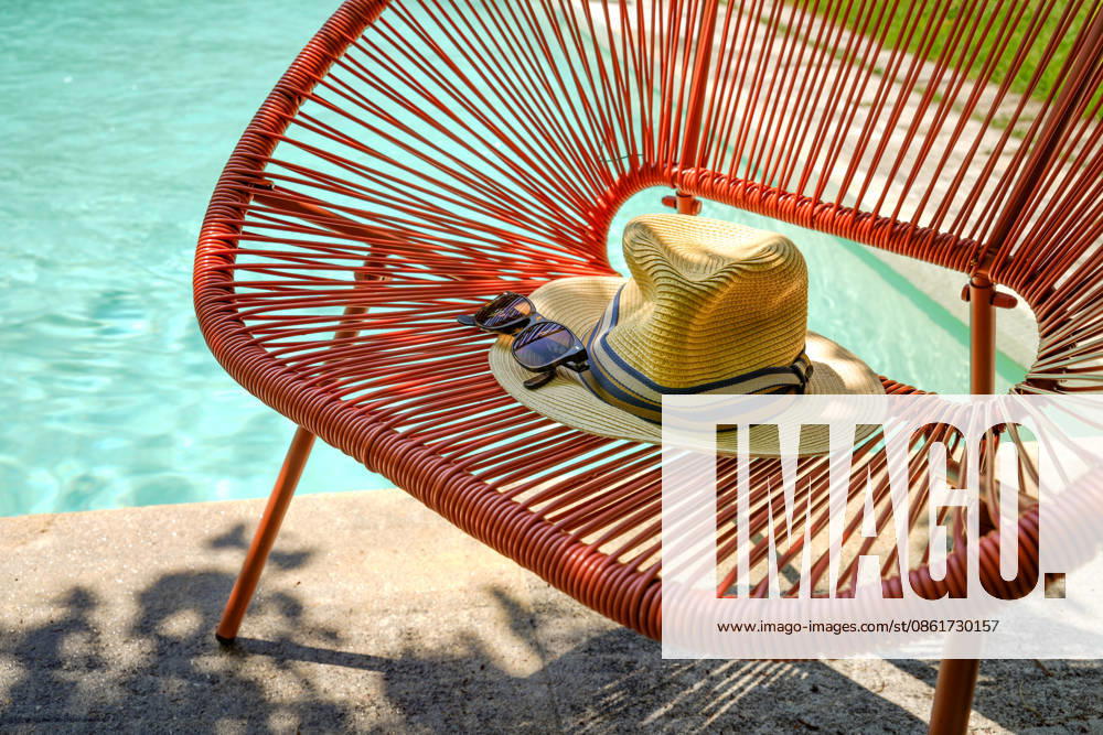 Sunny Scene on Pool edge Classic Summer Accessories like a Straw hat and a dark Sunglasses with striking Frame at a Bench at Acapulco Style 1133303198