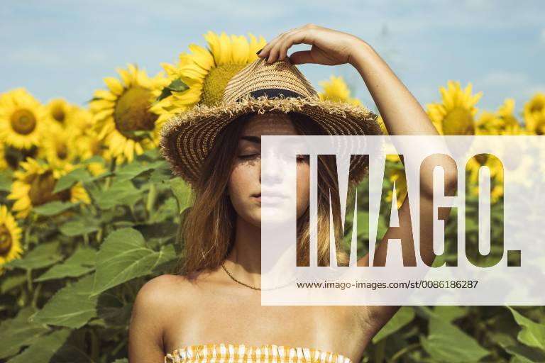 Young woman holding a straw hat on her head in a field of sunflowers model released Symbolfoto ACPF00325