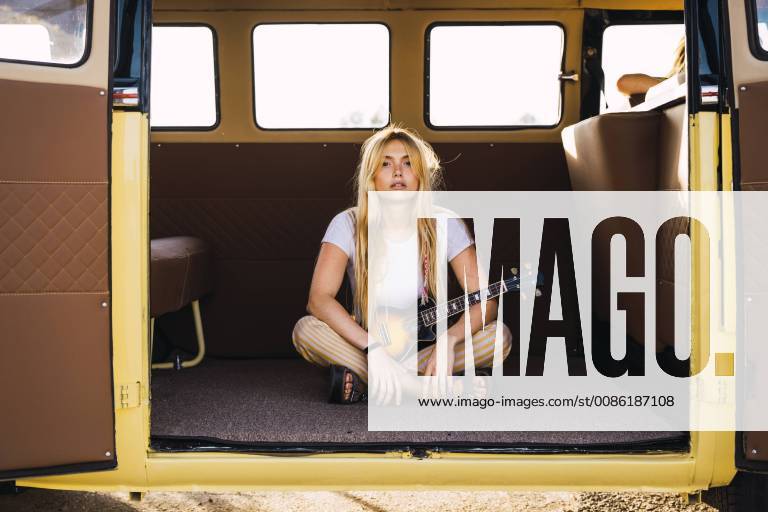 Young woman sitting in a van with a guitar model released Symbolfoto KKAF01368