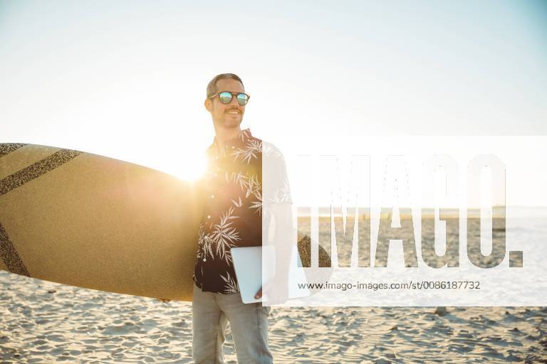 Man at the beach carrying surfboard and laptop model released Symbolfoto SUF00564
