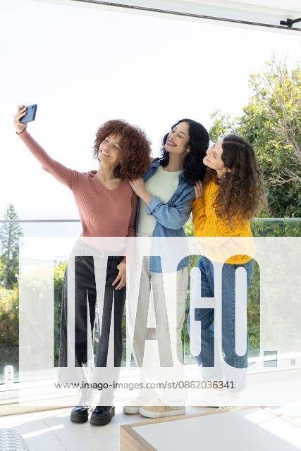 Diverse female friends posing for selfie on glass balcony overlooking water, holding smartphone, model released, property released, 02.09.2025 06:00:00, 8091131