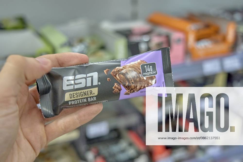 ESN Designer Protein Bar mit Schokoladengeschmack wird in der Hand gehalten, lila Verpackung, Supermarkt im Hintergrund, Produkt einkaufen, Drogerie Markt Laden, Rossmann, Deutschland ESN designer protein bar with chocolate flavor is held in hand, purple packaging, supermarket in the background, product shopping, drugstore store, Rossmann, Germany