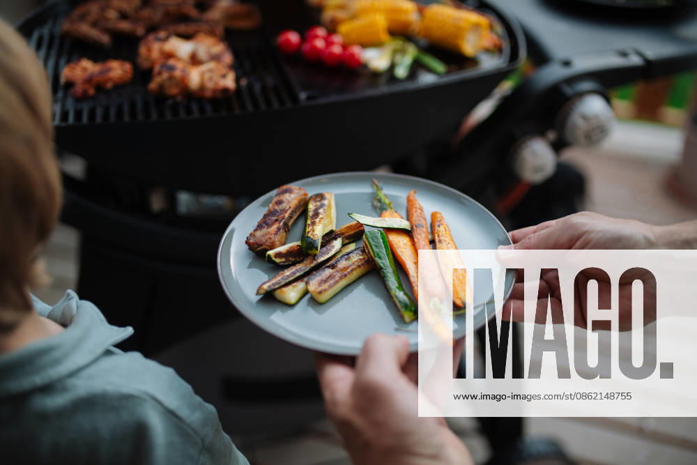 Father putting grilled meat and vegetable on plate to his son during family summer garden party. A father putting grilled meat and vegetable on plate to his son during family summer garden party. model released