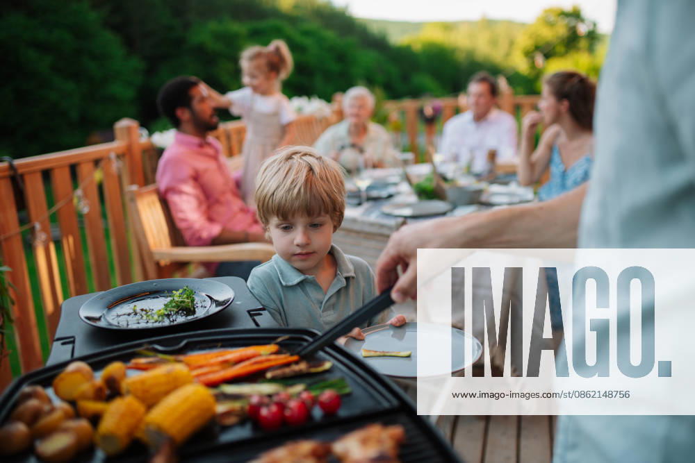Father putting grilled meat and vegetable on plate to his son during family summer garden party. A father putting grilled meat and vegetable on plate to his son during family summer garden party. model released