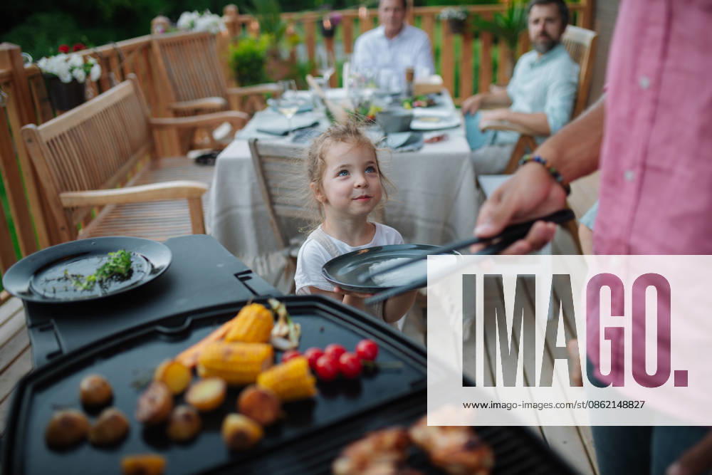 Father putting grilled meat and vegetable on plate to his son during family summer garden party. A father putting grilled meat and vegetable on plate to his son during family summer garden party. model released
