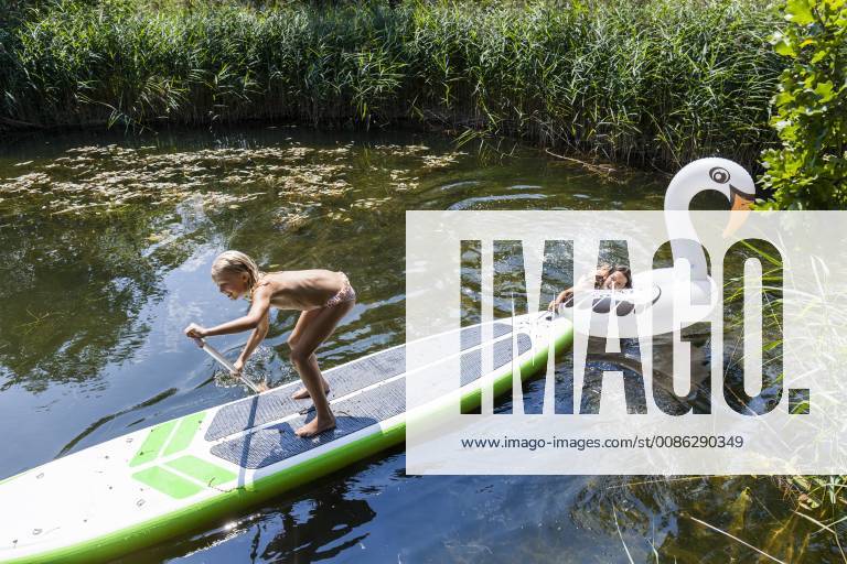 Two girls in a pond with inflatable pool toy in swan shape and SUP board model released Symbolfoto property released TCF05728