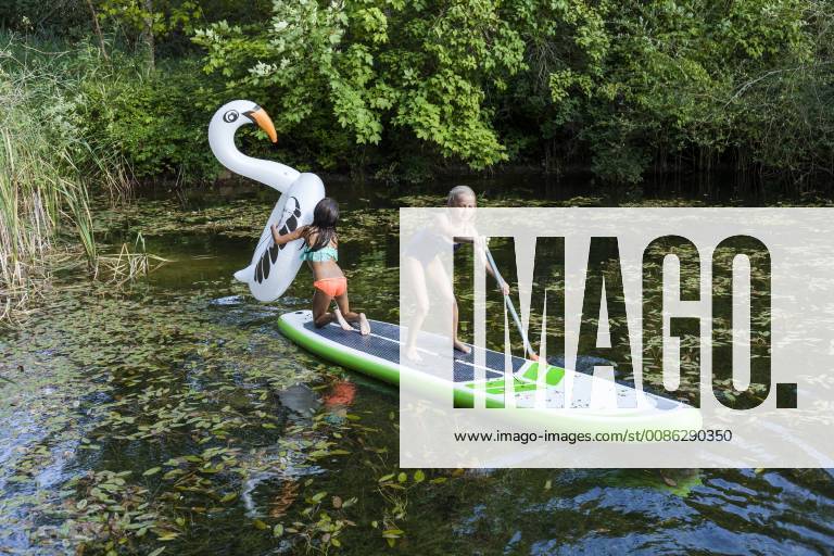 Two girls in a pond with inflatable pool toy in swan shape and SUP board model released Symbolfoto property released TCF05737