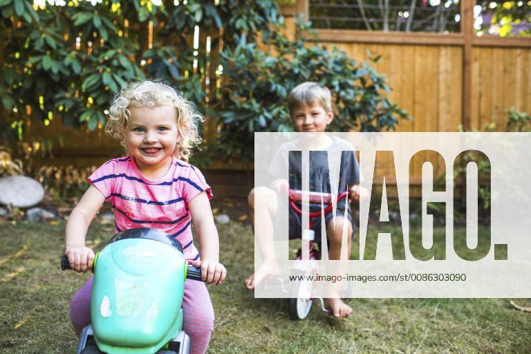 A smiling blond toddler girl in pink and a blond boy sit on tricycles in a backyard., SEATTLE Washington United States model released Symbolfoto