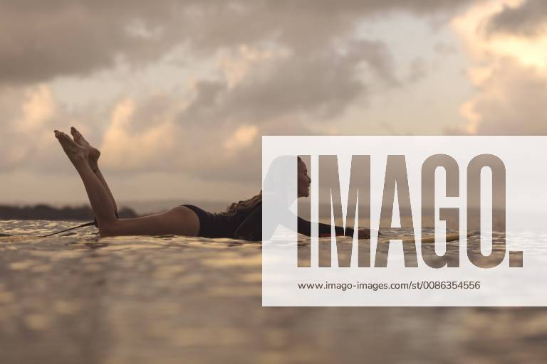 Female surfer lying on surfboard while surfing in ocean at dawn, Kuta, Bali, Indonesia, Kuta Bali Indonesia TRKO022967 model released Symbolfoto