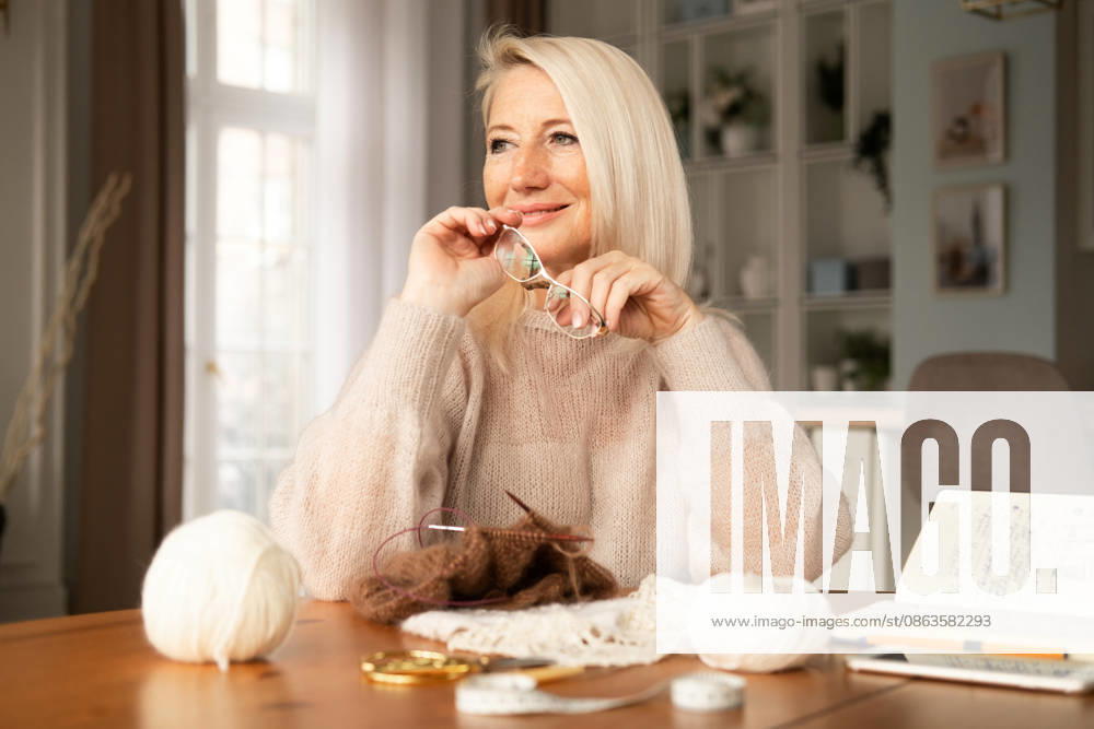 Eine glückliche, strahlende ältere Frau, die Stricknadeln in der Hand hält und lächelt, während sie einen Schal strickt Eine glückliche, strahlende ältere Frau, die Stricknadeln in der Hand hält und lächelt, während sie einen Schal strickt (License=RF) ,model released, Symbolfoto