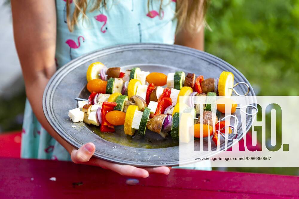 Girl holding plate with vegetarian grill skewers, tomato, yellow and green zucchini, tofu, feta, onion and champignon model released Symbolfoto SARF03931