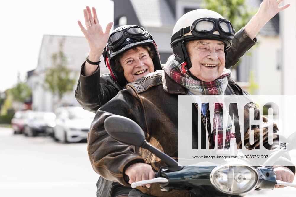 Happy senior couple having fun, riding motor scooter and waving model released Symbolfoto UUF14920