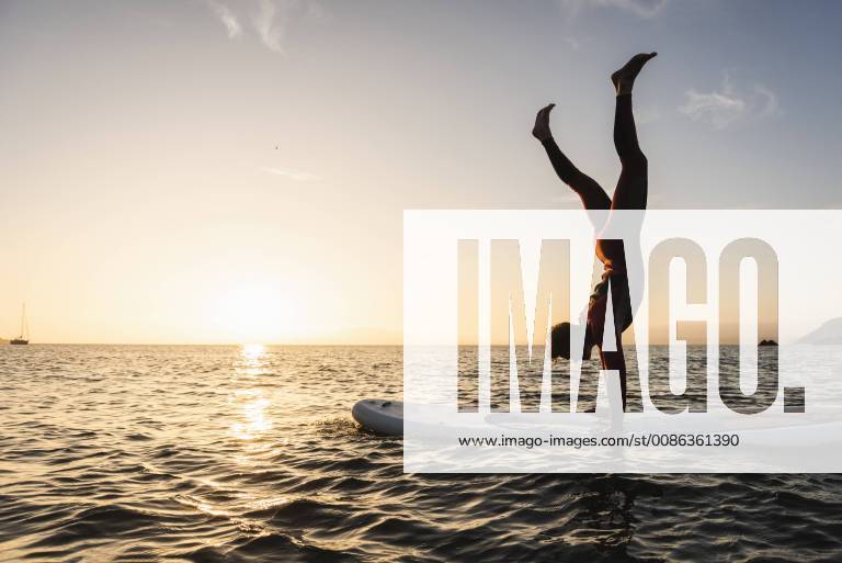Young man doing handstand on paddleboard at sunset model released Symbolfoto UUF15085