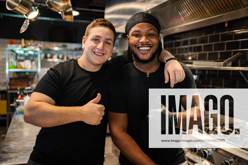 Fröhliche Mitarbeiter in einer Restaurantküche, die den Daumen hochhalten Two diverse friends smiling in professional kitchen showing approval (License=RF) ,model released, Symbolfoto