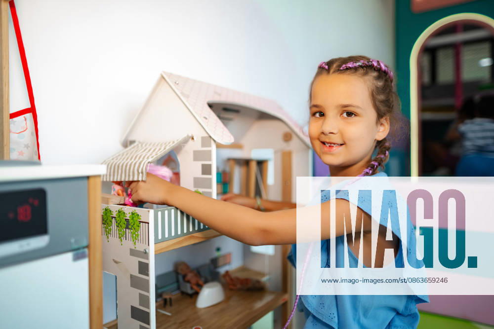 Ein kleines Mädchen spielt lächelnd mit einem Puppenhaus in einem Zimmer Young girl smiling during playtime, arranging dolls inside a toy dollhouse (License=RF) ,model released, Symbolfoto