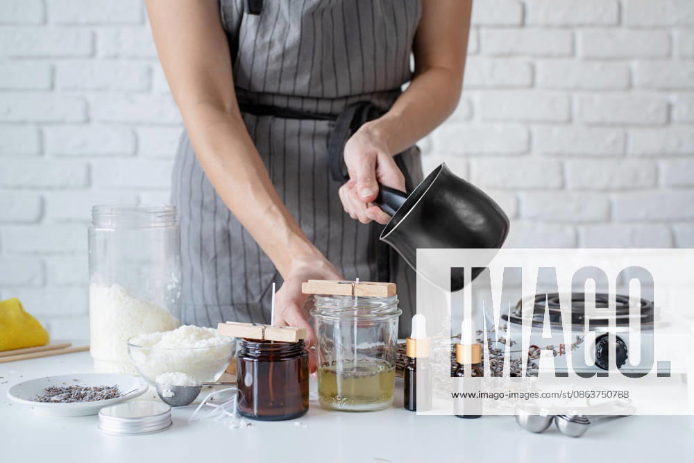 Frau beim Herstellen einer dekorativen Duftkerze am Tisch, Nahaufnahme Creative hobby at home. Woman making decorative aroma candle at table, poring melted soy wax into glass (License=RF) ,model released, Symbolfoto