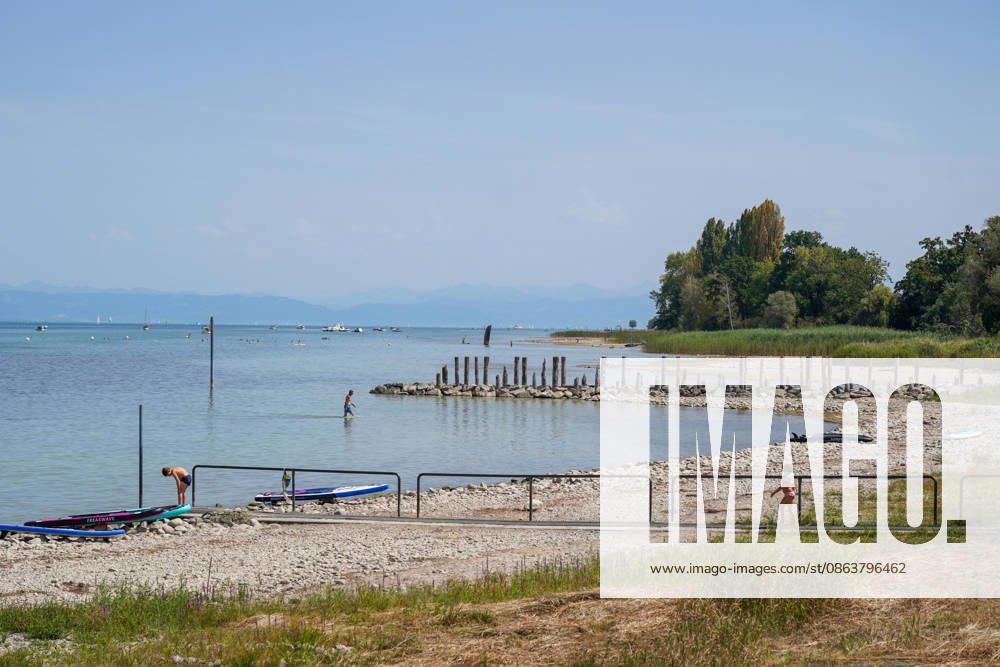 Switzerland, Lake Constance: Low water levels expose wide stretches of gravel and shoreline; swimmers stand in shallow water, SUP boards lie on the shore in the background; boats and an Alpine panorama. Stock image representing Lake Constance, water level, low water, drought, heat, heat wave, summer, climate change, bodies of water, shore, gravel beach