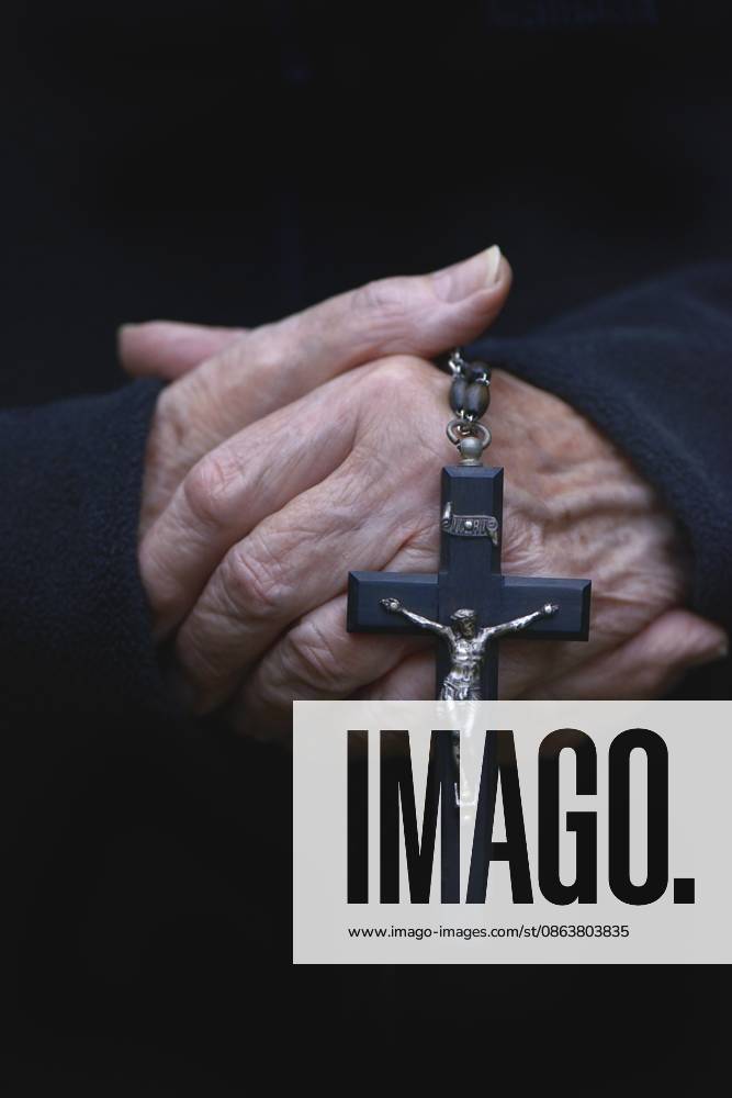 Hand hält Kruzifix vor dunklem Hintergrund Hand holding crucifix against dark background