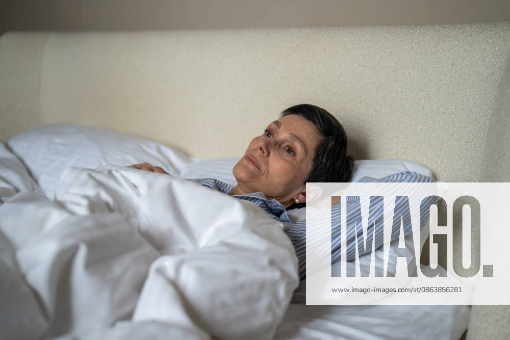 Eine unglückliche, nachdenkliche ältere Frau, die morgens zu Hause im Bett liegt und einen verlorenen, erschöpften Gesichtsausdruck hat. Unhappy thoughtful senior woman lying in bed in morning at home with lost exhausted expression, elderly female in bedroom showing loneliness and depression at older age, life after divorce. Melancholy (License=RF) ,model released, Symbolfoto