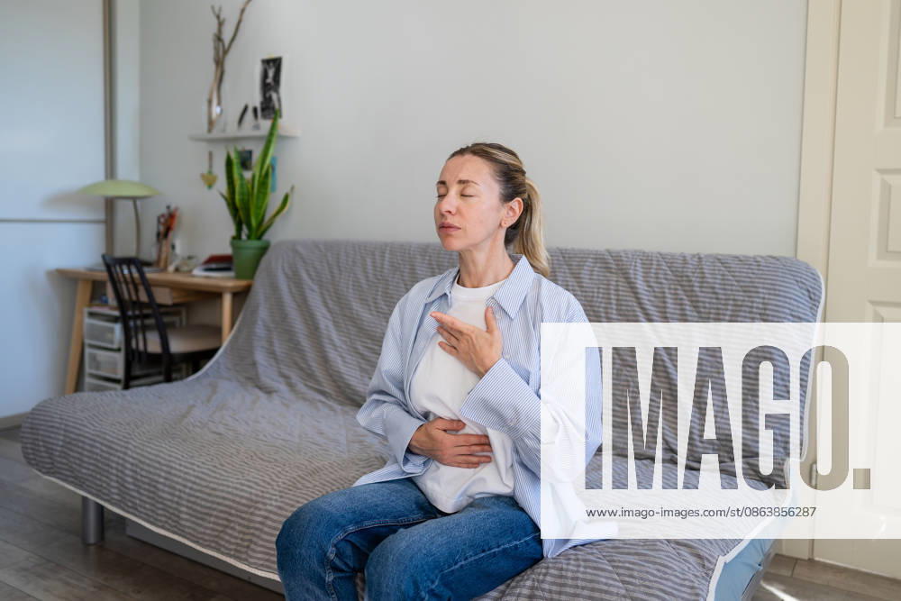 Eine positive, reife Frau, die zu Hause Selbsthilfetechniken zum Stressabbau und zur Tiefenatmung praktiziert. Calm mature woman do stress relief deep breathing self helping therapy, female sitting on sofa holding hands on chest inhaling air, focusing on physical and mental relaxation, healing zen practice (License=RF) ,model released, Symbolfoto