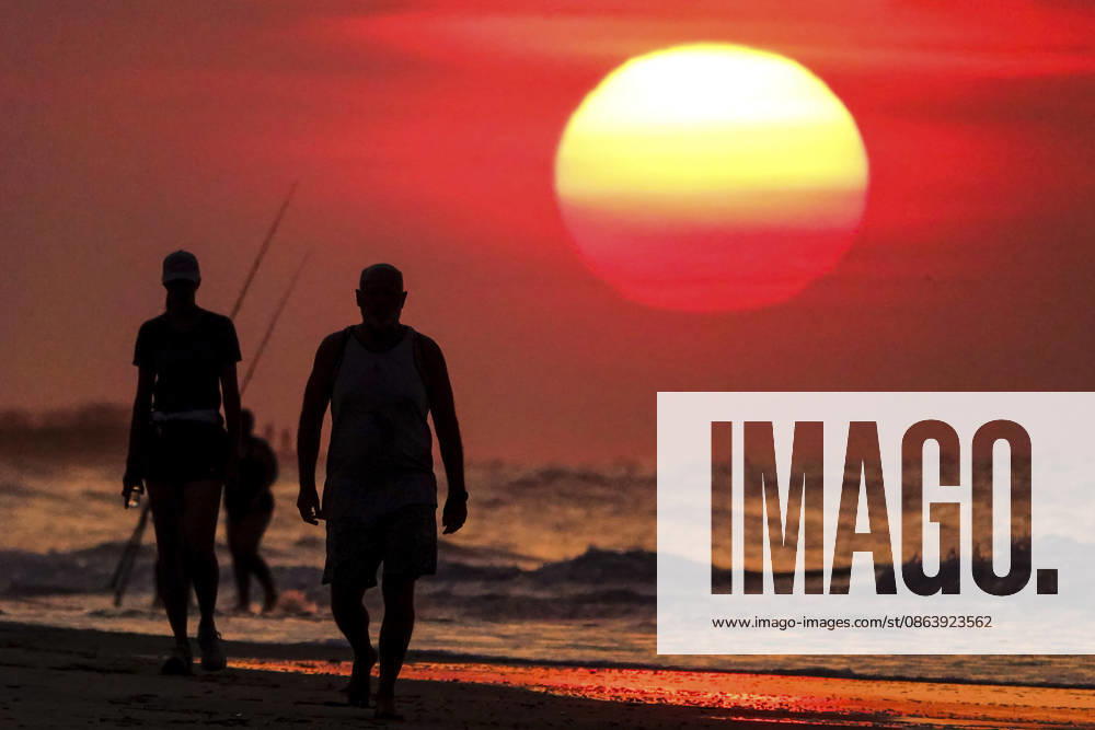 People silhouetted by the sunrise, walk along the beach as the massive ball rises over the Atlantic Ocean, August 12, 2026 in Isle of Palms, South Carolina. The Charleston area is currently under a heat advisory with temperatures in the 90â€⠢s and a heat index of 115-degrees. Isle Of Palms United States - ZUMAe02_ 20260812_zaf_e02_005
