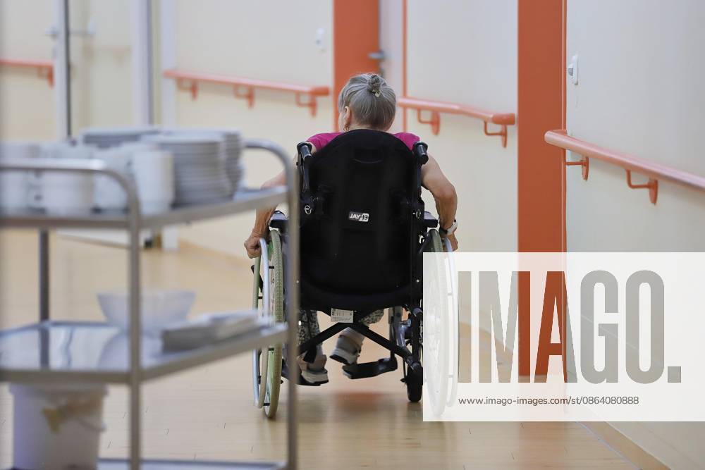 An elderly woman is being pushed in a wheelchair through a nursing home
