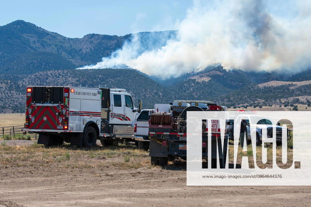 A plume of thick smoke rises into the sky above a mountain ridge as the Big Mountain Fire burns southwest of Elberta, Utah, United States, on August 23, 2026. A line of emergency response vehicles can be seen staged along a dirt road below the active wildland blaze. Elberta USA - ZUMAm292 20260823_znp_m292_001