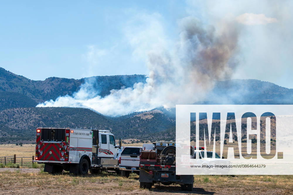 A plume of thick smoke rises into the sky above a mountain ridge as the Big Mountain Fire burns southwest of Elberta, Utah, United States, on August 23, 2026. A line of emergency response vehicles can be seen staged along a dirt road below the active wildland blaze. Elberta USA - ZUMAm292 20260823_znp_m292_002