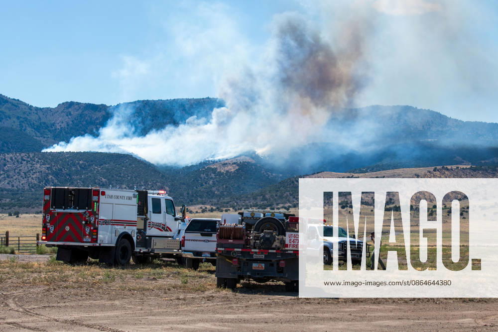 A plume of thick smoke rises into the sky above a mountain ridge as the Big Mountain Fire burns southwest of Elberta, Utah, United States, on August 23, 2026. A line of emergency response vehicles can be seen staged along a dirt road below the active wildland blaze. Elberta USA - ZUMAm292 20260823_znp_m292_003