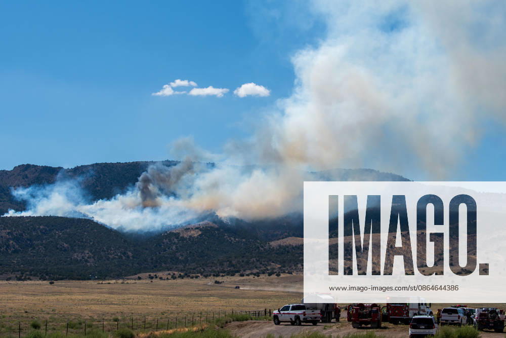 A plume of thick smoke rises into the sky above a mountain ridge as the Big Mountain Fire burns southwest of Elberta, Utah, United States, on August 23, 2026. A line of emergency response vehicles can be seen staged along a dirt road below the active wildland blaze. Elberta USA - ZUMAm292 20260823_znp_m292_007
