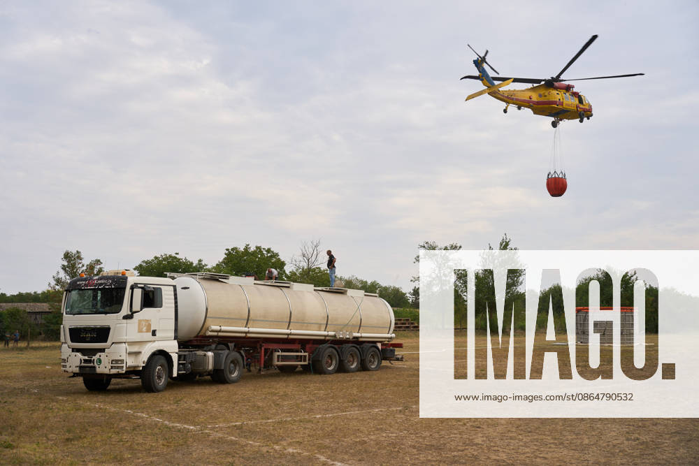 2026825, Susara, Serbia - Two Sikorsky UH-60 Black Hawk helicopters are deployed to the village of Susara to help battle the severe wildfires devastating the Deliblato Sands (Deliblatska Pescara) Special Nature Reserve, refilling their buckets from a large portable water tank placed on a local football pitch. Susara Serbia - ZUMAd223 20260825_zip_d223_011