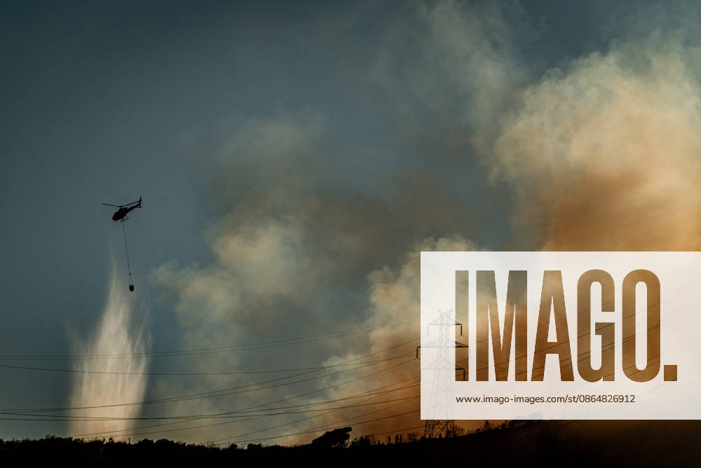 A helicopter drops water on a wildfire burning in the Collserola mountain range in Barcelona as thick smoke rises over the hills. The fire has affected the city s Nou Barris district, prompting authorities to evacuate and shelter residents in the Torre Baro and Ciutat Meridiana neighborhoods. Barcelona Spain - ZUMAb137 20260825_fap_b137_017