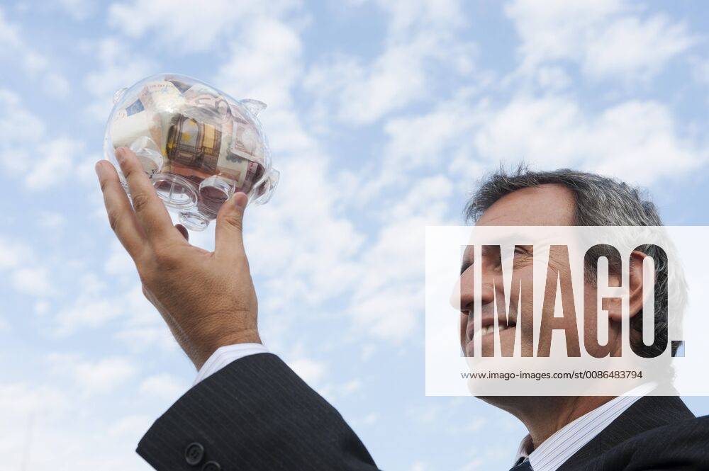 Mature man holding up transparent piggy bank filled with euros