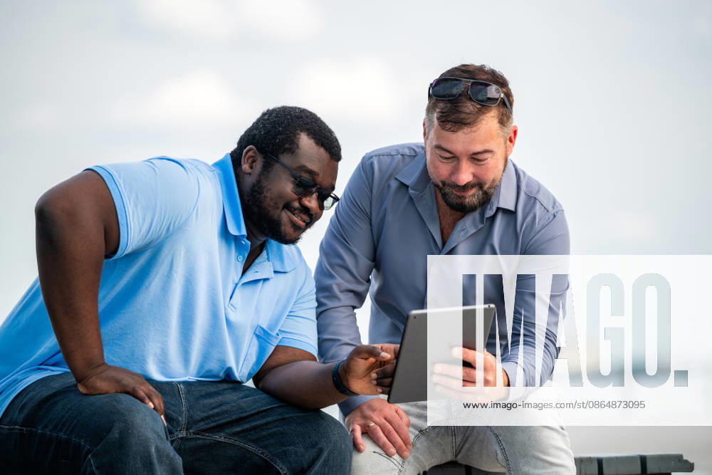 Two diverse male friends using a digital tablet outdoors Saint Petersburg, Saint Petersburg, Russia CR_YFCG260824-2080923-01 ,model released, Symbolfoto ,property released