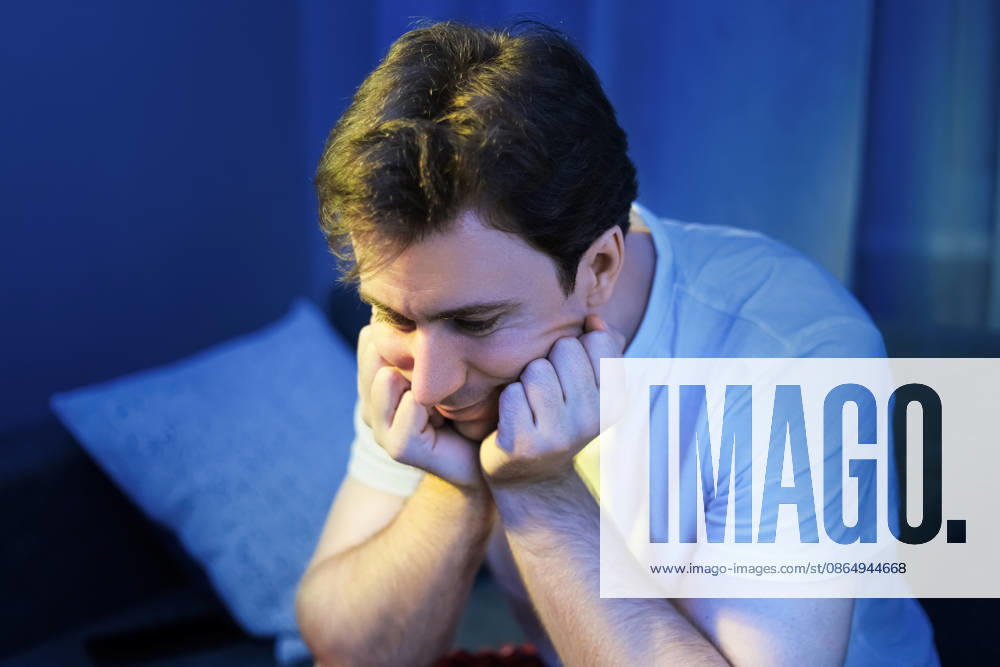 Ein trauriger, niedergeschlagener und besorgter Mann, der nachts unter Schlaflosigkeit leidet. Ein müder und einsamer Mensch, der gestresst vor einem leuchtenden Bildschirm sitzt. Sad, depressed, and worried man suffering from insomnia at night. Tired and lonely person sitting stressed in front of a glowing screen. High quality photo (License=RF) ,model released, Symbolfoto