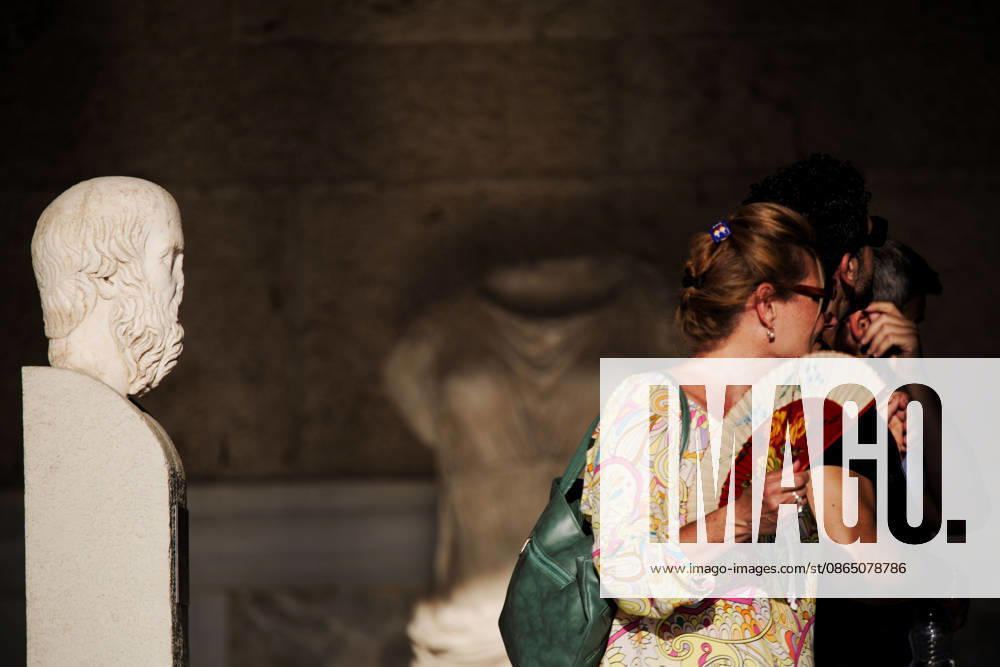 A tourist uses a hand fan to cool herself next to an ancient statue while visiting the Stoa of Attalos at the Ancient Agora of Athens during hot summer weather. Athens Greece - ZUMAthen 20260827_mda_x103_782