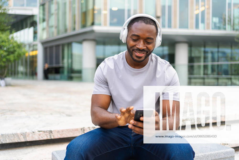 Musik-Song-Konzept. Ein guter Start in den Tag. Ein fröhlicher Afroamerikaner, der einen modernen Hit hört und Spaß auf den Straßen der Stadt hat. Ein junger, gutaussehender Mann mit Kopfhörern, der es genießt, seine Lieblingsmusik auf dem Handy zu hören. Musik-Song-Konzept. Guten Starttag. Glücklicher afrikanischer amerikanischer Mann hören modernen Hit auf der Straße in der Stadt. Personen, die Kopfhörer tragen, genießen das Zuhören Lieblingsmusik am Telefon. Menschen Lifestyle Freude (License=RF) ,model released, Symbolfoto