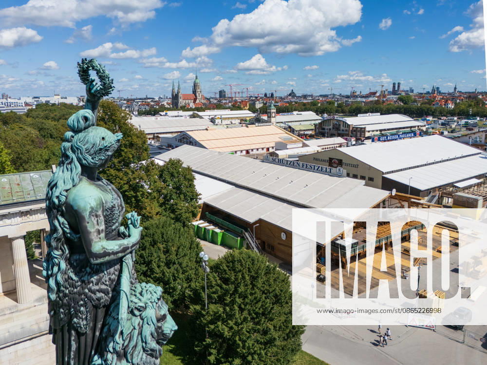 – Die Bavaria-Statue blickt auf die Aufbauarbeiten für das Oktoberfest: Die Bavaria-Statue steht neben ihrem Löwen und blickt während der Aufbauphase des Oktoberfestes 2026 auf die Theresienwiese. Unten erheben sich große Bierzelte wie das Schützenfestzelt und das Paulaner-Festzelt zwischen Holzkonstruktionen und auf dem