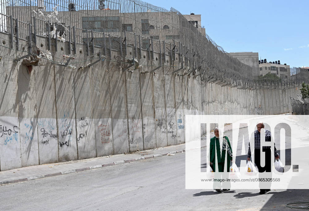 Palestinians carry groceries beside the Israeli separation wall that cuts through Beit Hanina in East Jerusalem on Sunday, August 30, 2026. Thousands of Palestinian residents of East Jerusalem are forced to go through time consuming checkpoints to reach their schools, jobs, hospitals and visit family because of the separation barrier. JER2026083004 DEBBIExHILL