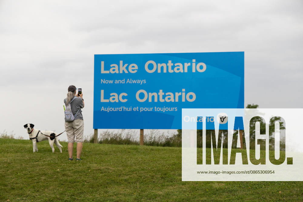(260830) -- HAMILTON, Aug. 30, 2026 -- A woman takes photos of an English-French bilingual sign reading Lake Ontario Now and Always at a lakeside conservation area in Hamilton, Ontario, Canada, on Aug. 30, 2026. Canadian Prime Minister Mark Carney said Thursday that the name Lake Ontario carries a long history and that Canadians will always use this name regardless of external changes. The Canadian prime minister made the remarks after U.S. President Donald Trump signed an executive order earlier on Thursday, directing the Department of the Interior to rename the lake Lake America, as trade tensions between the United States and Canada have been escalating. (Photo by Xinhua) CANADA-ONTARIO-HAMILTON-LAKE ONTARIO-NAME ZouxZheng
