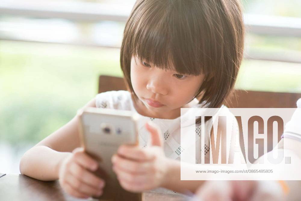 Asian child playing smart phone at cafe. Natural light outdoor lifestyle. model released Symbolfoto