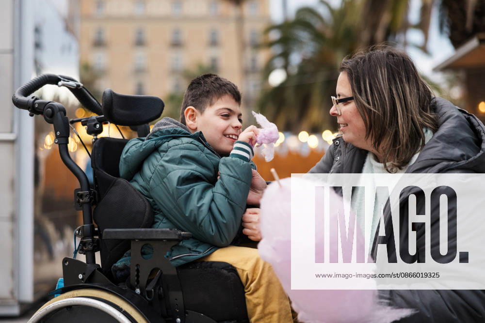Mother and son in wheelchair eat cotton candy at outdoor market, JMIF00152