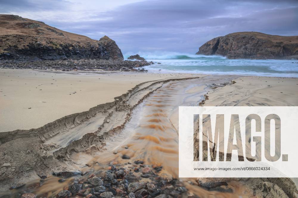Bachläufe durchziehen den Sandstrand, während Wellen gegen Felsen prallen, Schottland, Großbritannien Stream carving patterns through sandy beach as waves crash against rocks, Scotland, United Kingdom