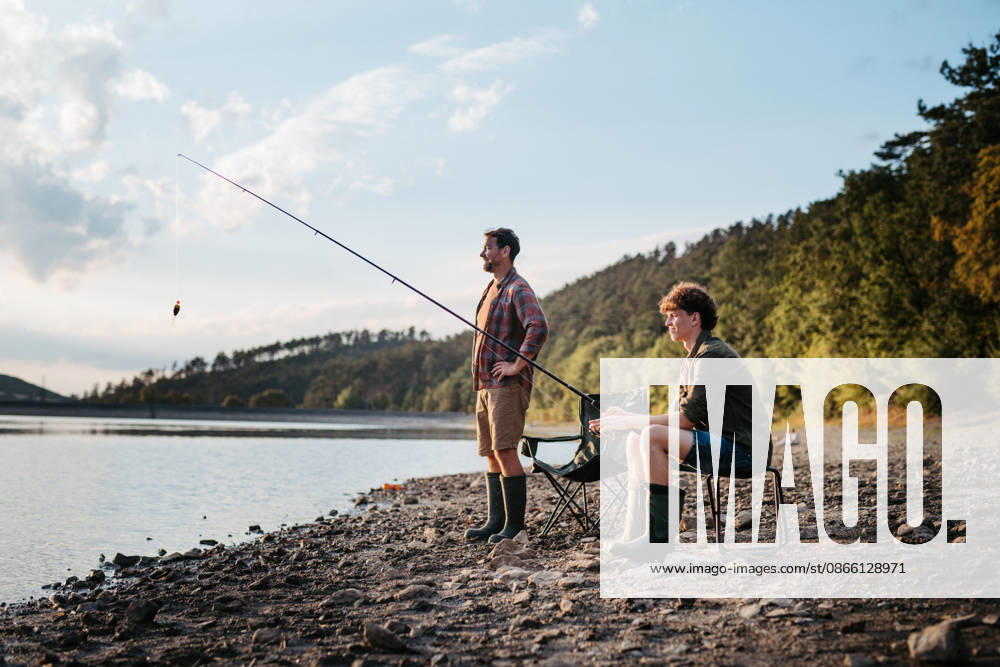 Father teaching teenage son to fish during outdoor trip. Teenage boy learning how to fish from his father. model released