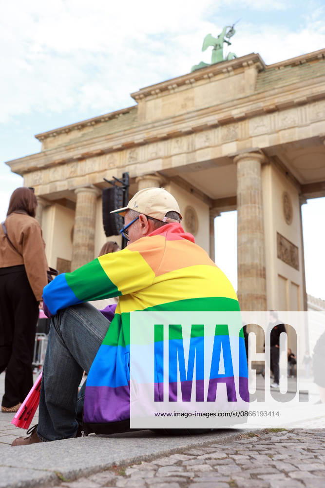 A participant wearing a rainbow-colored jacket waits for the rally to begin. The event, held under the slogan Time to Act: Stop the AfD, is taking place in Berlin at the Branden