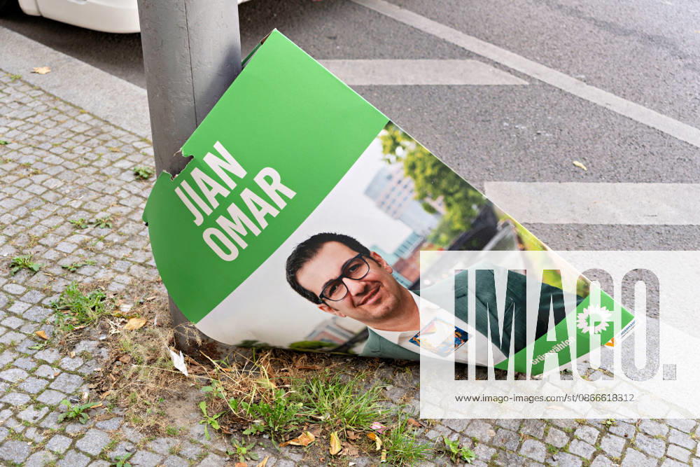 A damaged campaign poster for Green Party candidate Jian Omar lies at the base of a pole on the sidewalk in Berlin. A fallen Green Party campaign poster on the side of the road in Berlin