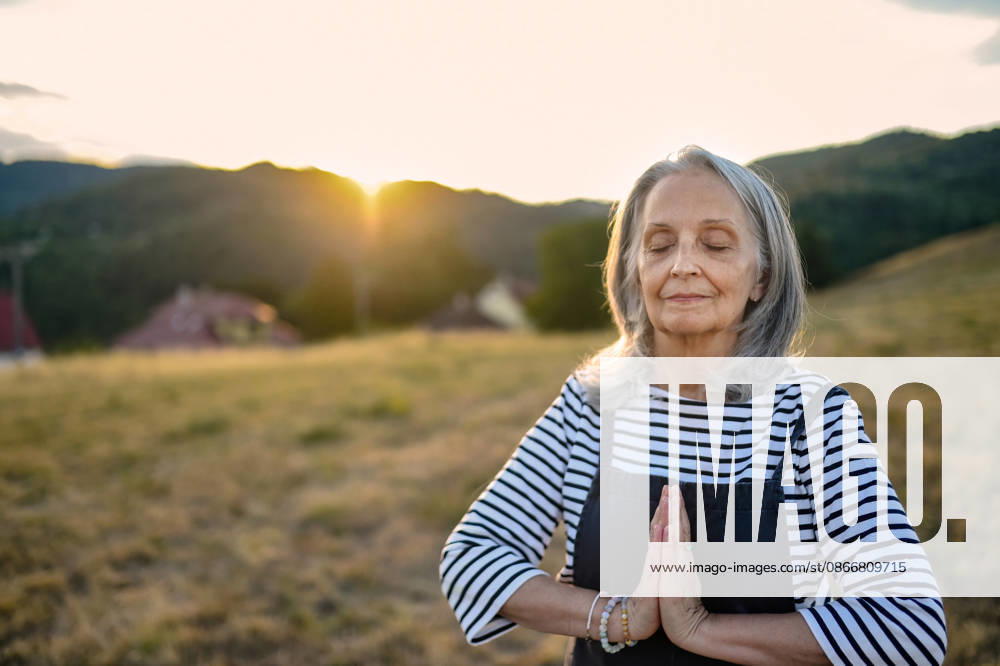 Senior woman practicing meditation outdoors in peaceful countryside. Senior woman taking care of body and mind during outdoor wellness routine. model released