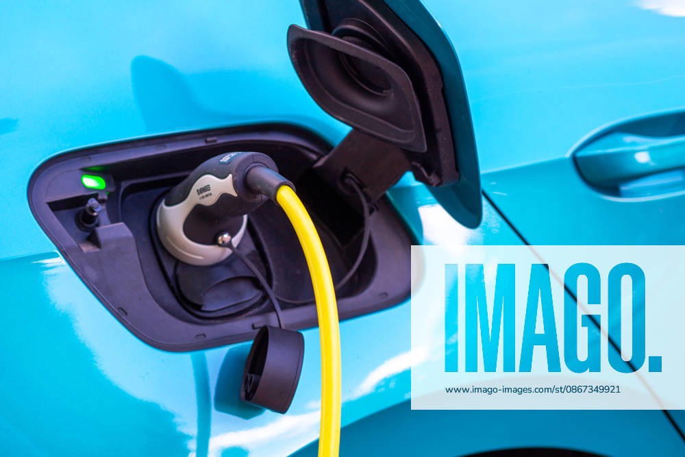 Close-up of the charging port on a turquoise electric car, with a yellow charging cable featuring a Type 2 Mennekes plug plugged into it