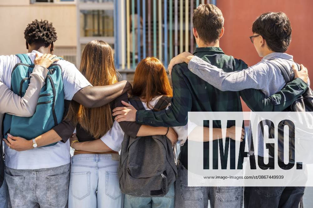 Gruppe multiethnischer Schüler, die mit umeinander geschlagenen Armen im Freien stehen und Freundschaft, Vielfalt und Zusammengehörigkeit in einem pädagogischen Umfeld symbolisieren Group of multi ethnic students standing outdoors with arms wrapped around each other, symbolizing friendship, diversity, and togetherness in an educational setting